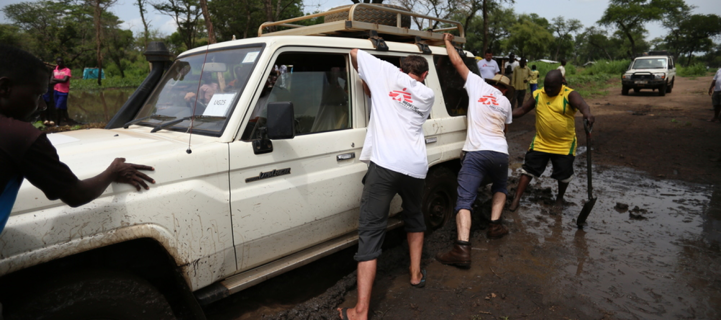 Bewohner eines Camps in Uganda helfen unserer Mitarbeitern, einen Wagen aus dem Matsch zu ziehen. Geflüchtete Uganda Teamarbeit Geländewagen